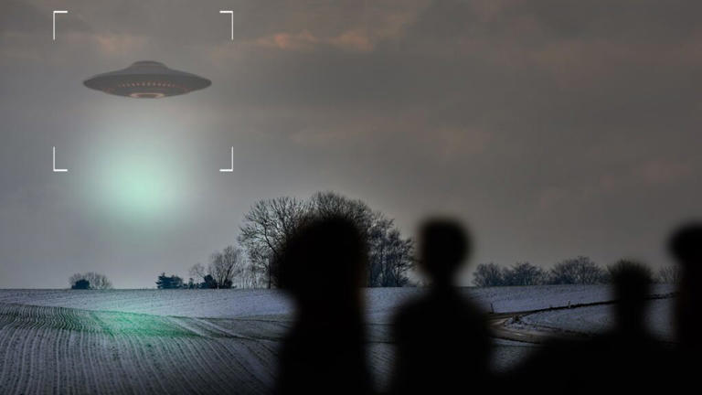 A UFO hovers in a cloudy sky above a snowy field, silhouetted figures in the foreground watch