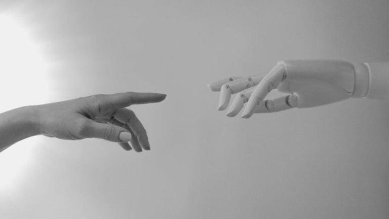 A human hand and a robotic hand reach towards each other against a light gray background
