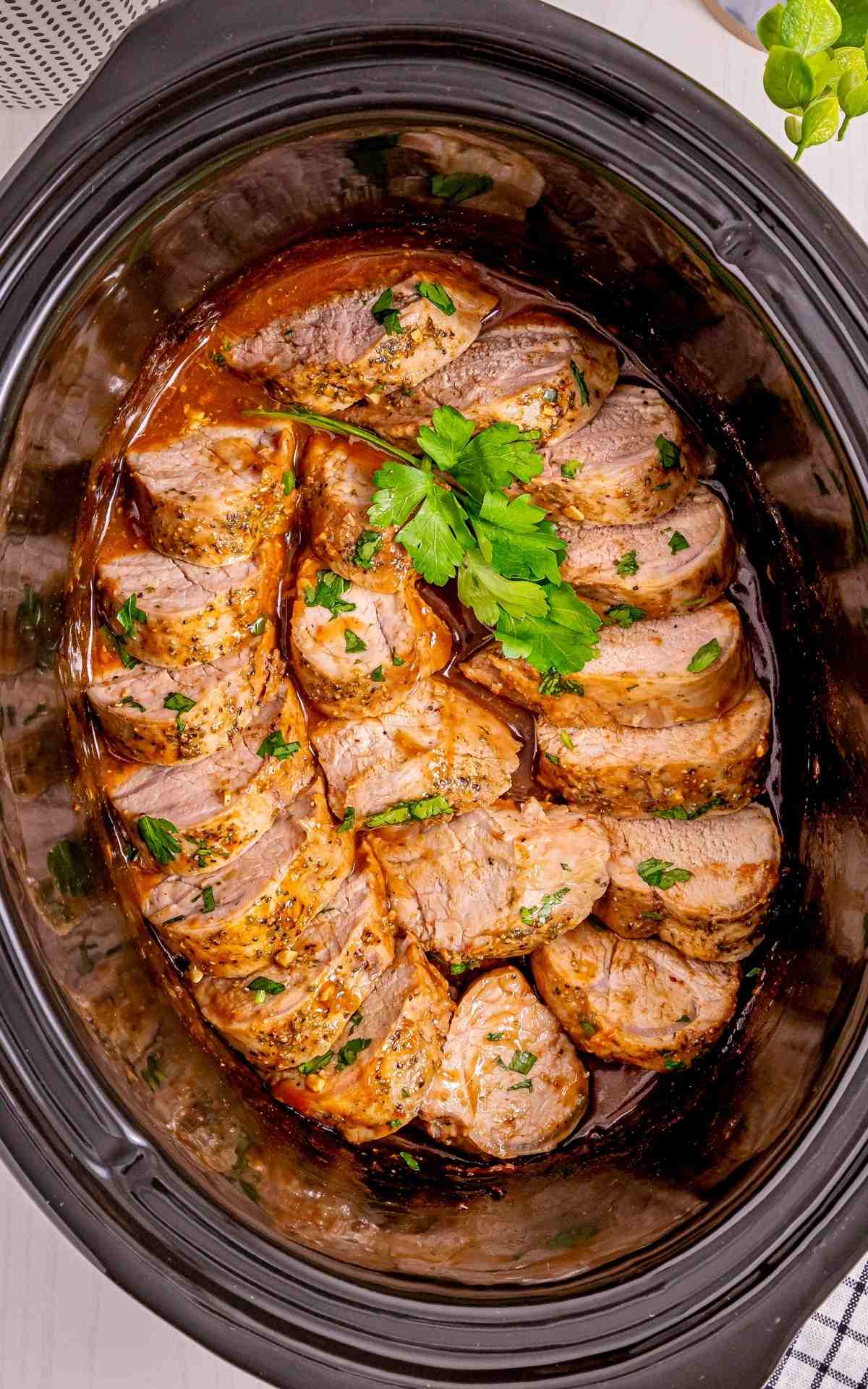 A Crock Pot with sliced pork tenderloin in sauce.