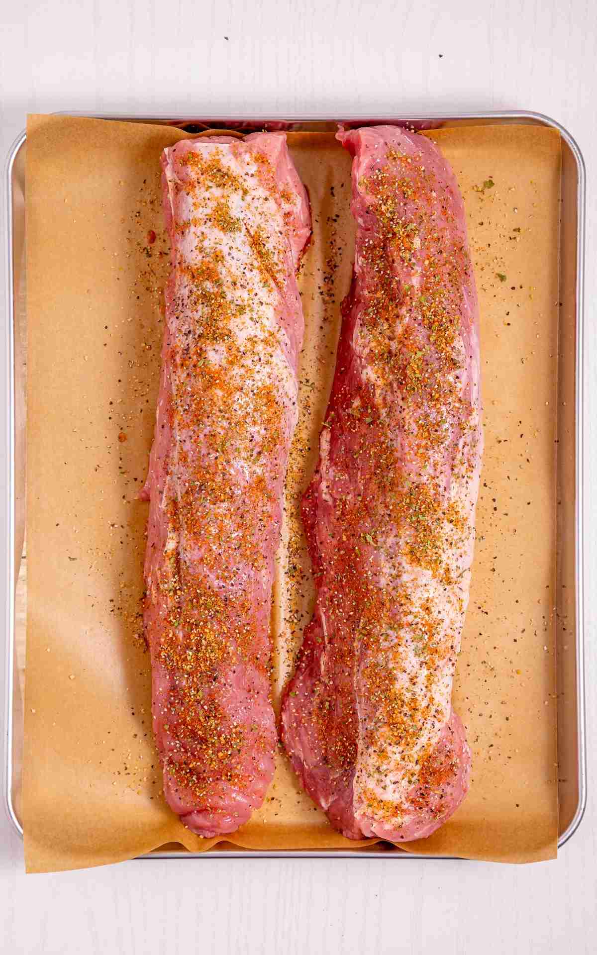 Two pork tenderloins dry rubbed resting on parchment.