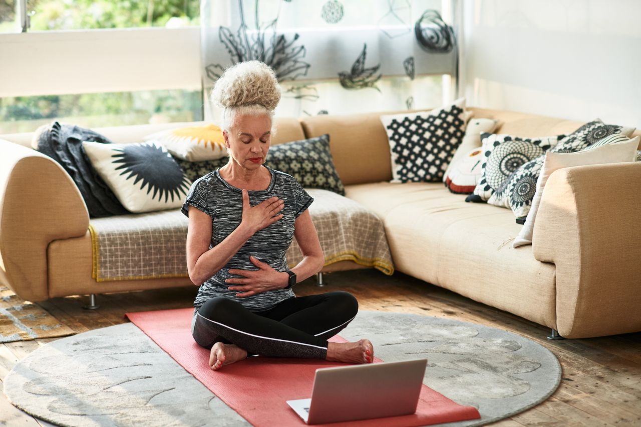 Senior woman with eyes closed meditating, sitting cross-legged on floor, control, breathing, zen, serene people