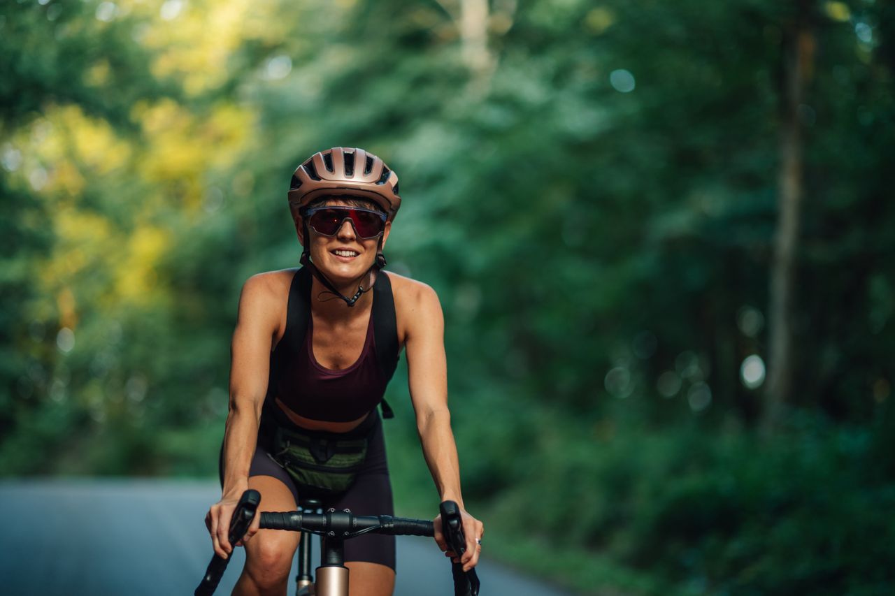 Young woman cyclist wearing helmet and sunglasses riding a bicycle on a forest road, enjoying the fresh air and nature