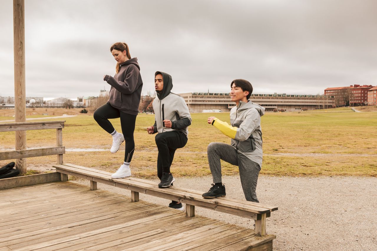 Three friends cheering each other on as they do step ups at an outdoor gym.