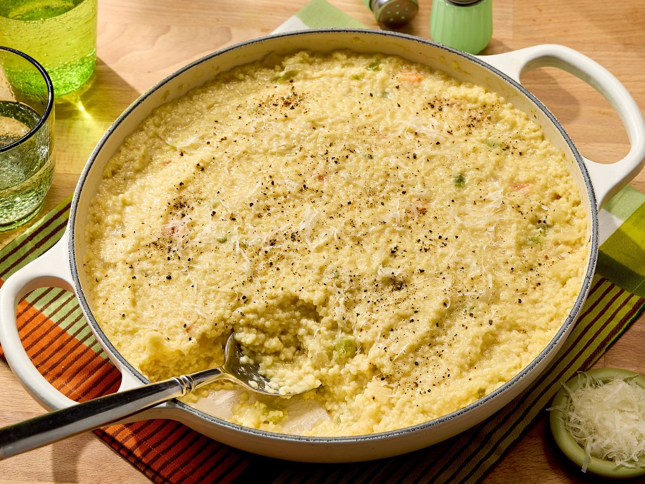 A dish of baked pasta casserole on a table with a spoon placed in it surrounded by tableware