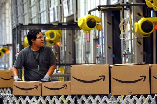 A worker watches as boxed merchandise moves along a conveyor belt to a waiting truck for delivery at the Amazon.com Phoenix Fulfillment Center in Goodyear, Arizona, U.S., on Monday, Nov. 16, 2009. Seattle-based Amazon.com, which started as a book seller, has expanded to products such as food and motor parts as it tries to become a general merchandiser. Photographer: Joshua Lott/Bloomberg via Getty Images