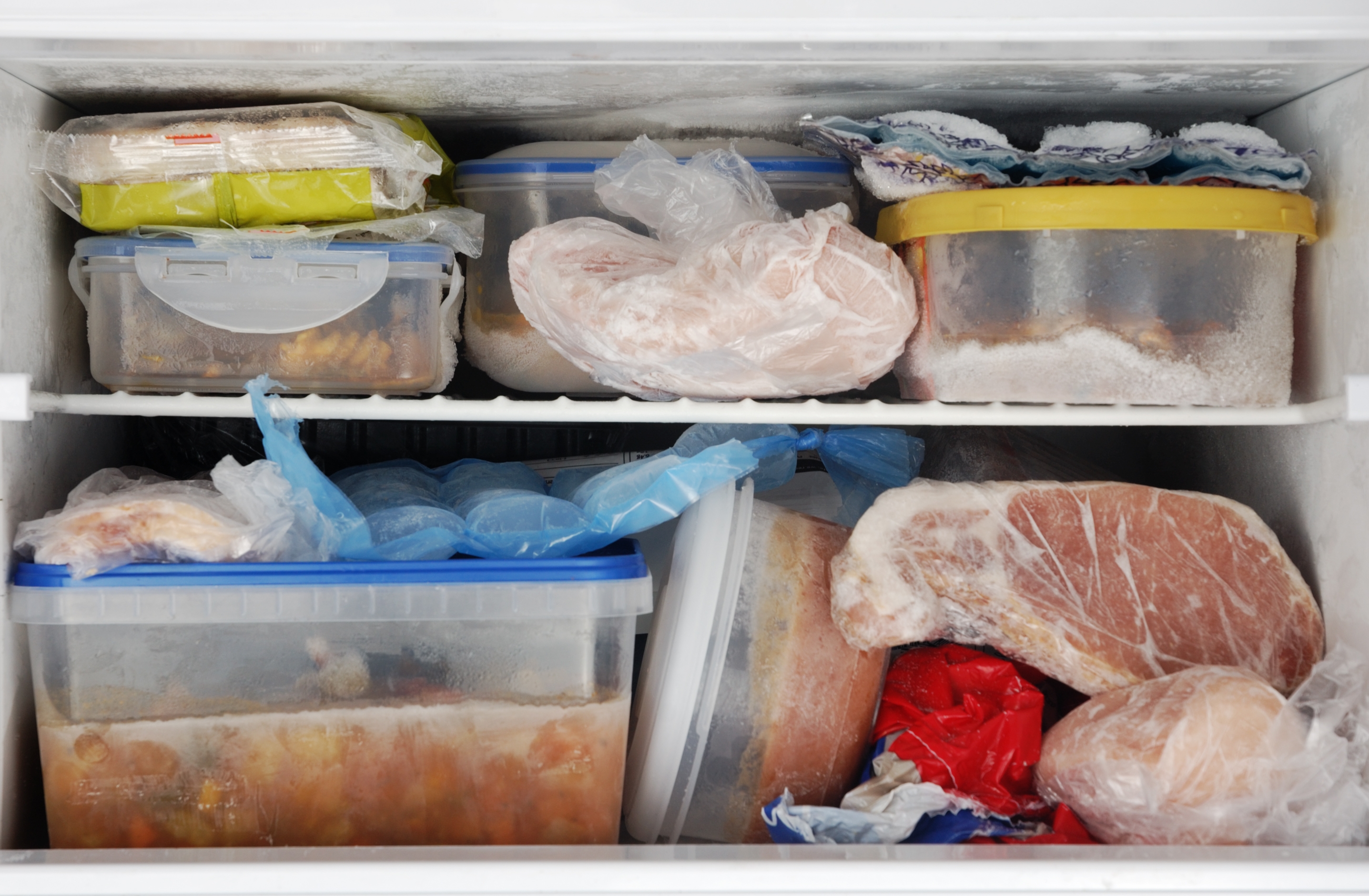 Freezer filled with various food items, including meats and plastic containers, organized on two shelves