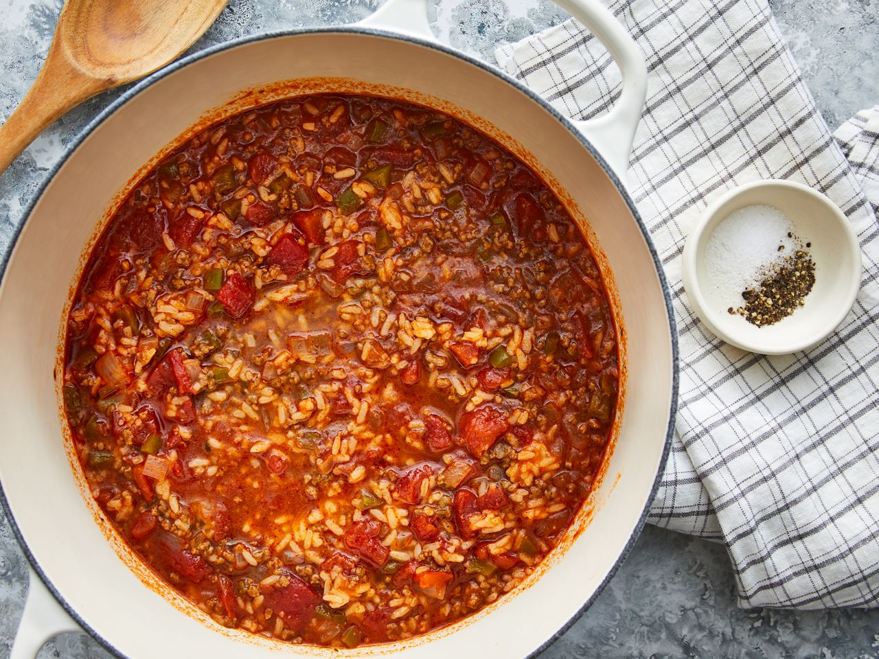 looking down at a large pot full of stuffed pepper soup with rice, next to kitchen towels and a wooden spoon