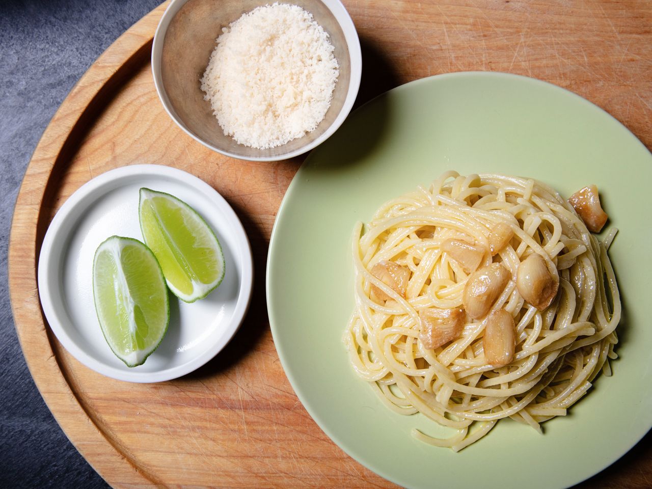 Overhead view of a plate of garlic pasta with grated cheese and lime wedges alongside.