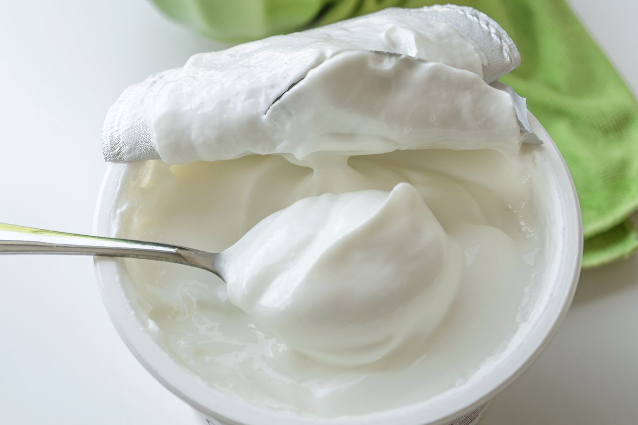 A spoon in a container of yogurt with the lid partially peeled back