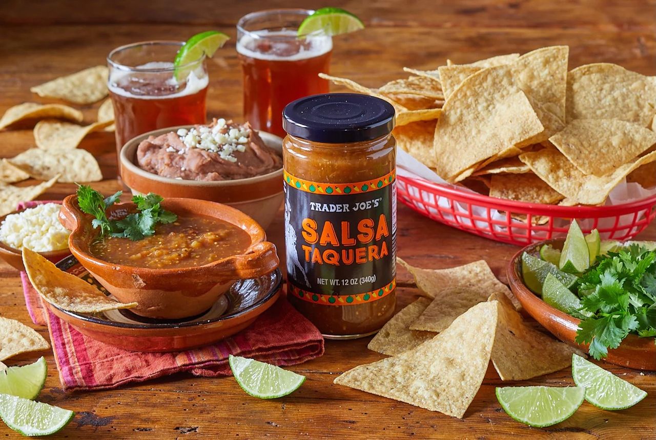 Jar of salsa with chips dips and lime wedges on a wooden table