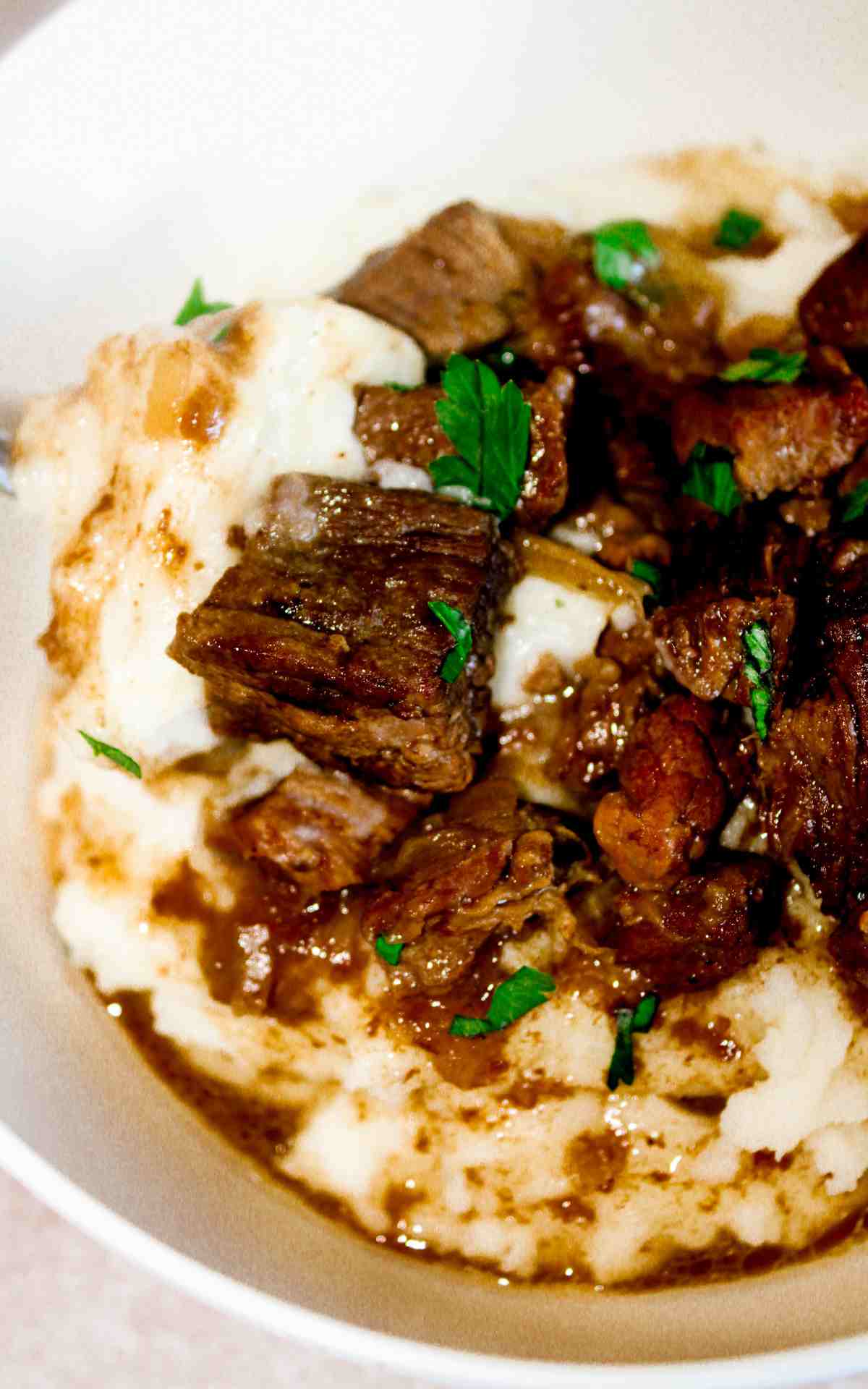 Close up of a white bowl of slow cooker beef tips with gravy.