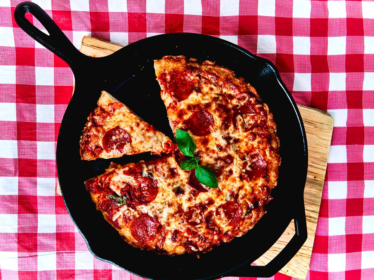 overhead view of cast iron skillet pepperoni pizza on red check tablecloth