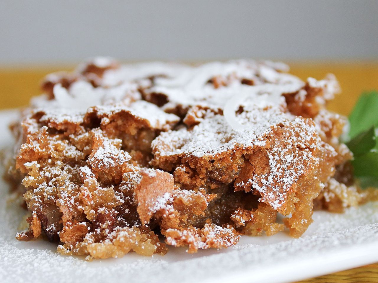 close up view of a slice of Sad Cake garnished with powdered sugar and greens on a white plate