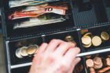 Eine Hand greift in eine Kasse voll Bargeld.