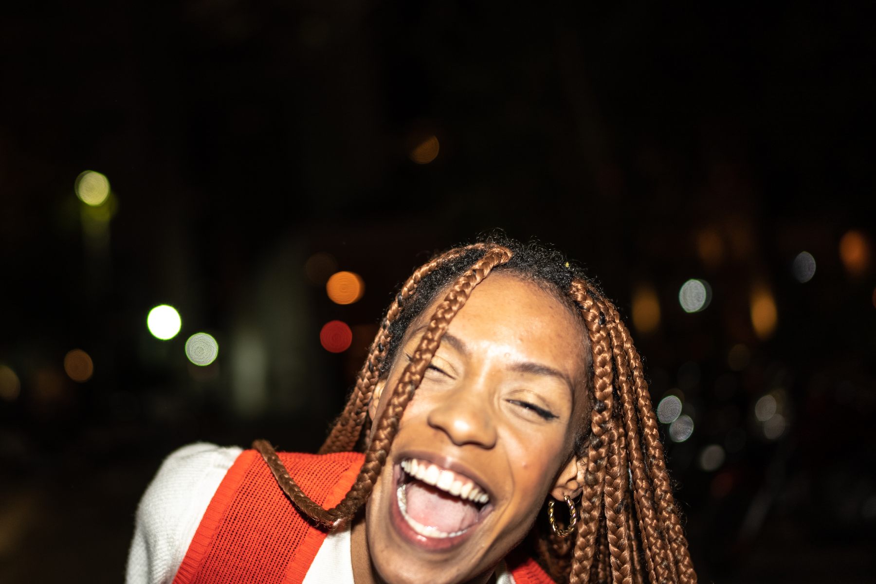 Image of a young Black woman laughing against a dark background with blurry lights.