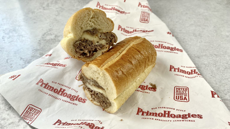The Philly Cheesesteak from PrimoHoagies cut in half on top of the take-out wrapping paper.