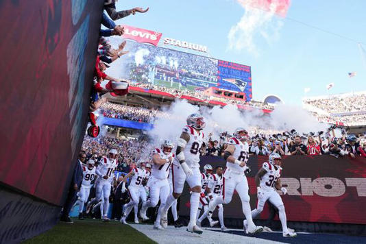 A group of athletes, dressed in white uniforms, is emerging from the tunnel onto the field, with smoke effects and a cheering cr