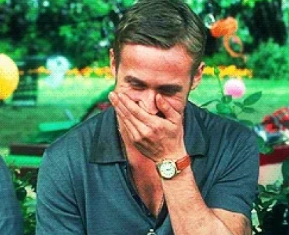 Person sitting outdoors, laughing with hand over mouth, wearing a casual shirt and watch, surrounded by blurred greenery and balloons in the background