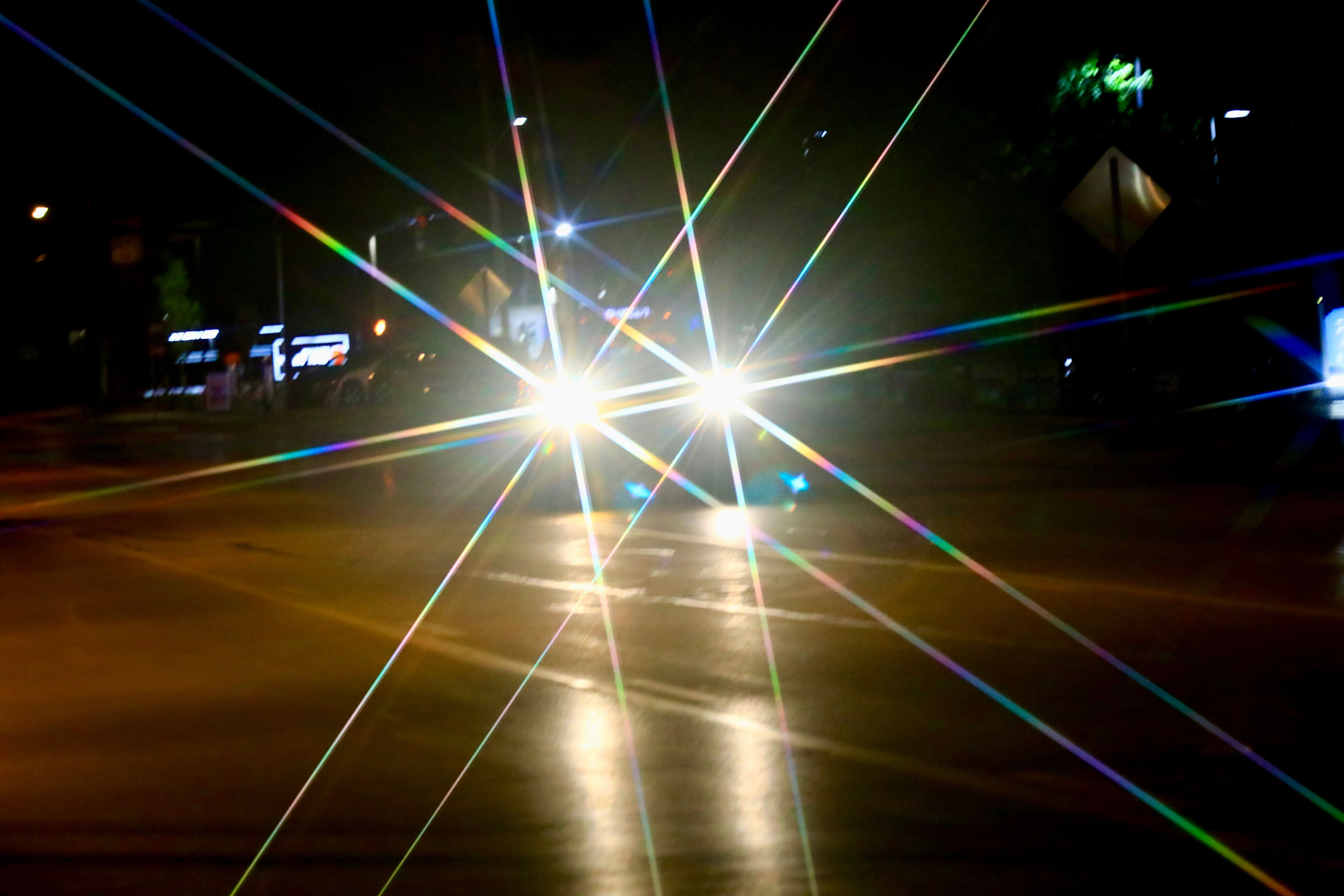 Headlights of a car in the dark create starburst patterns, highlighting the effect of bright light at night