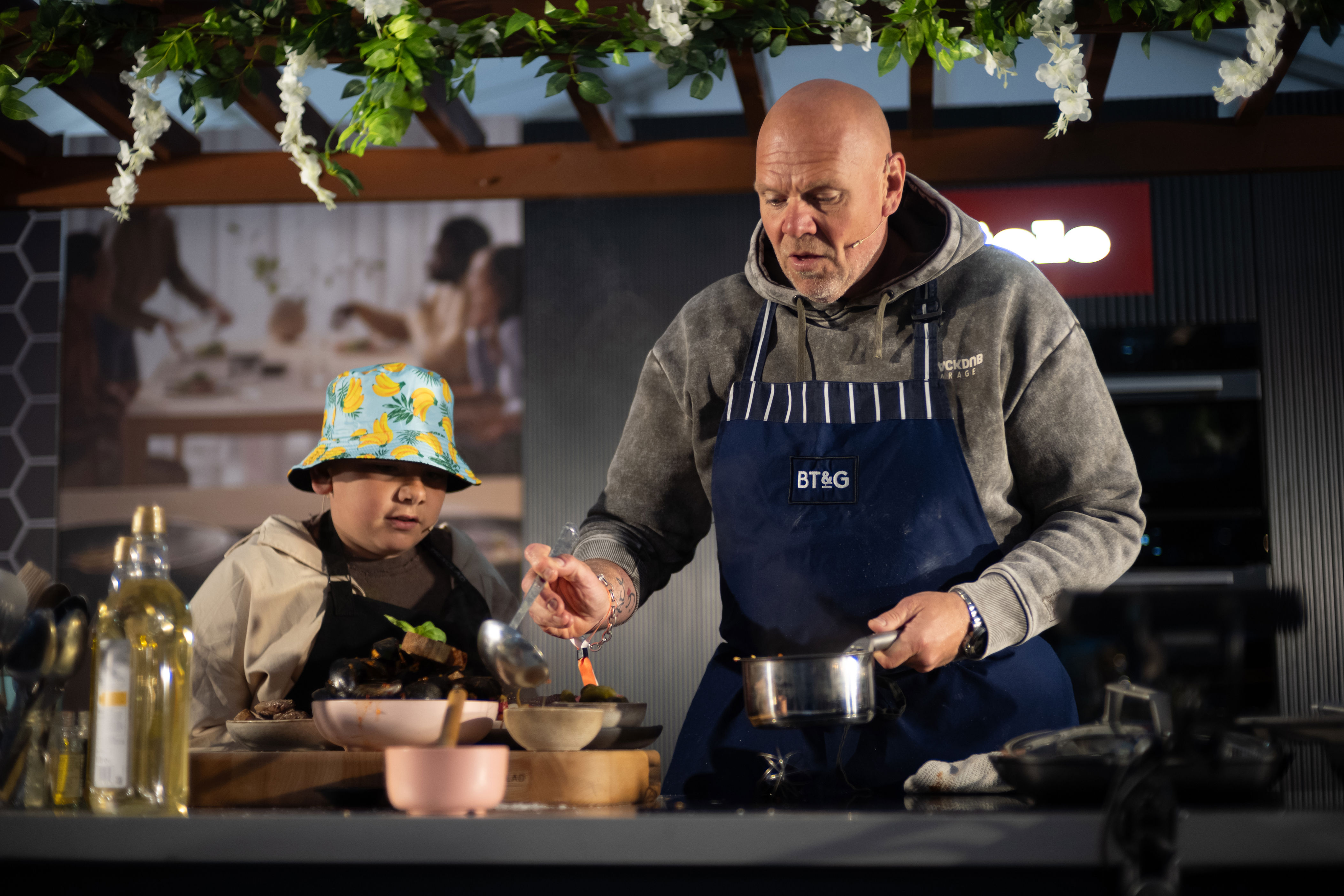 Shot of Tom Kerridge and son Acey cooking together in an outdoor kitchen for a charity gala