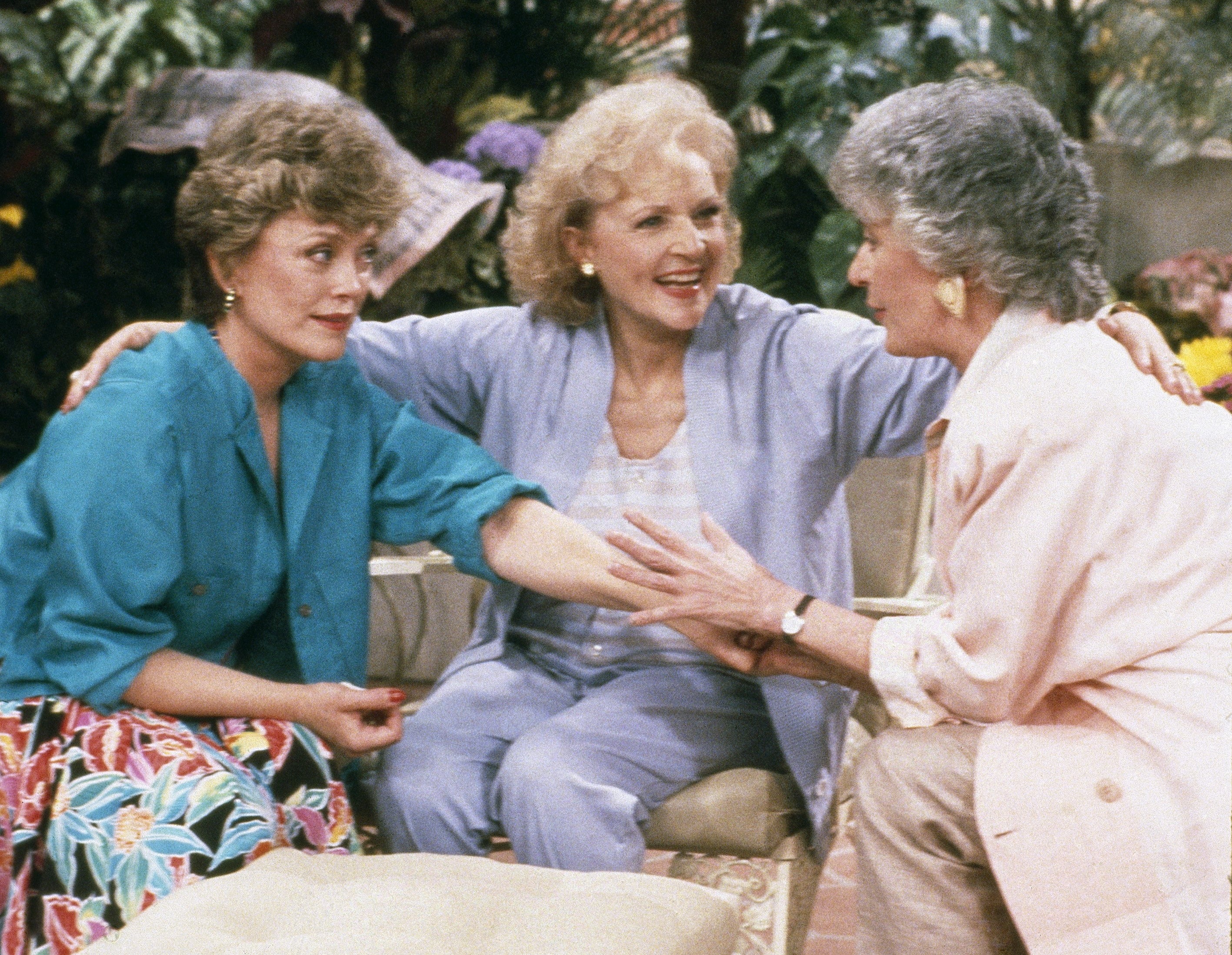 Three women sit together outdoors, smiling and chatting