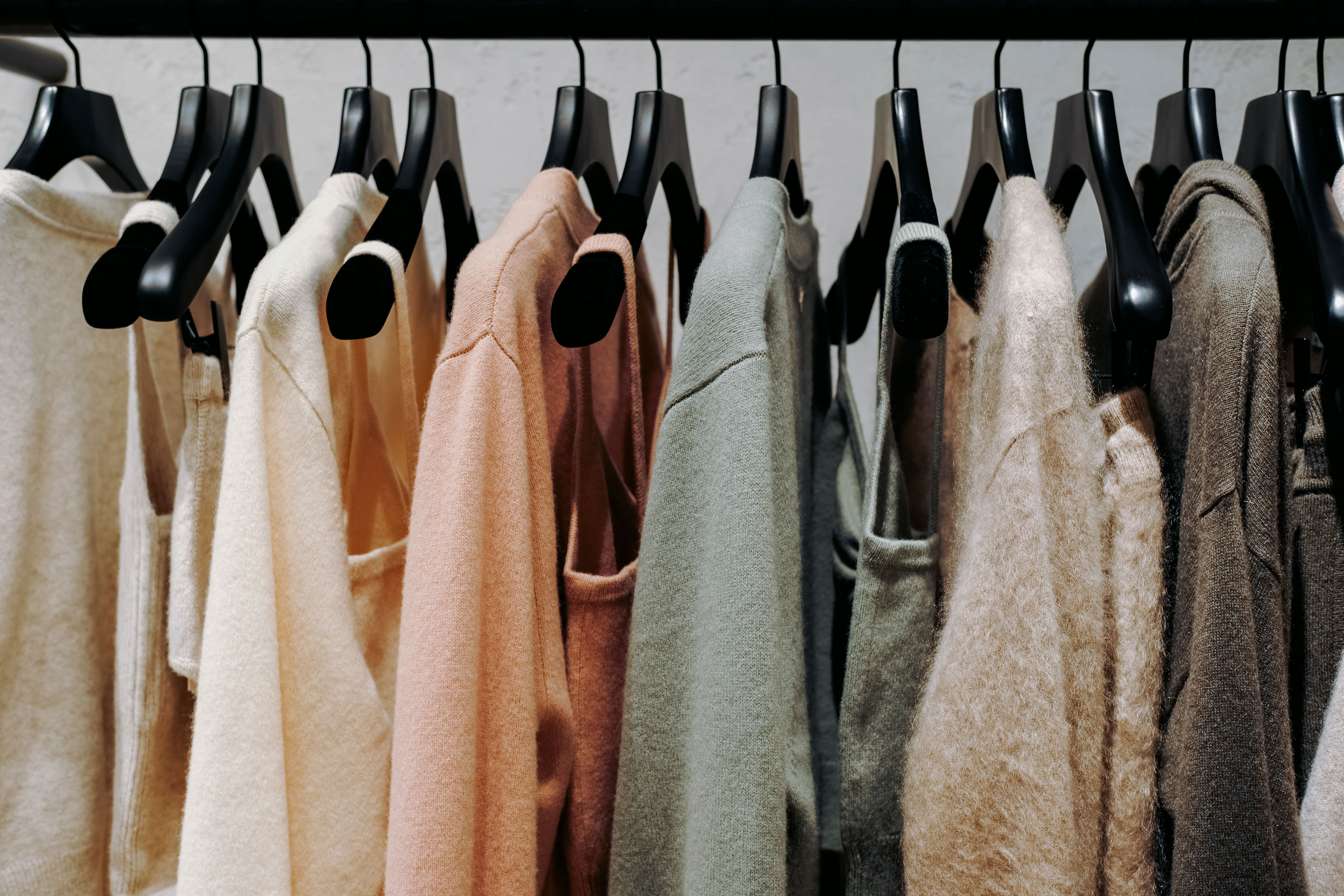 Clothing rack with various cozy sweaters in neutral and pastel shades, neatly arranged on black hangers