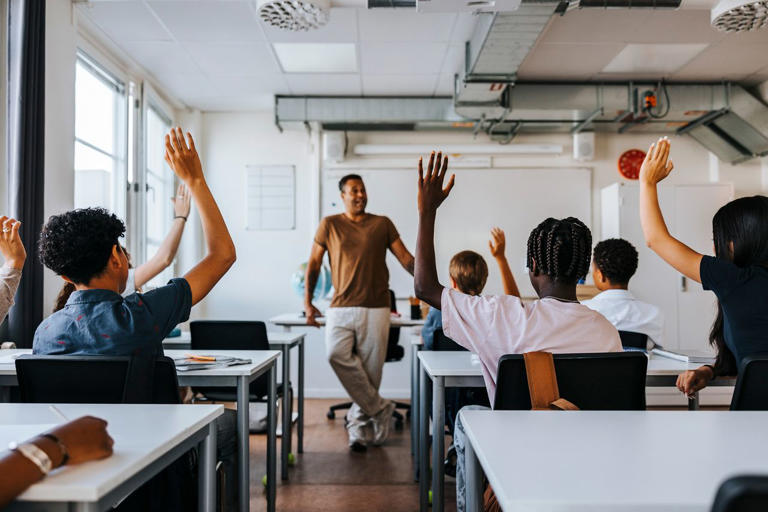 A classroom of kids raising their hands. Maskot/Getty Images
