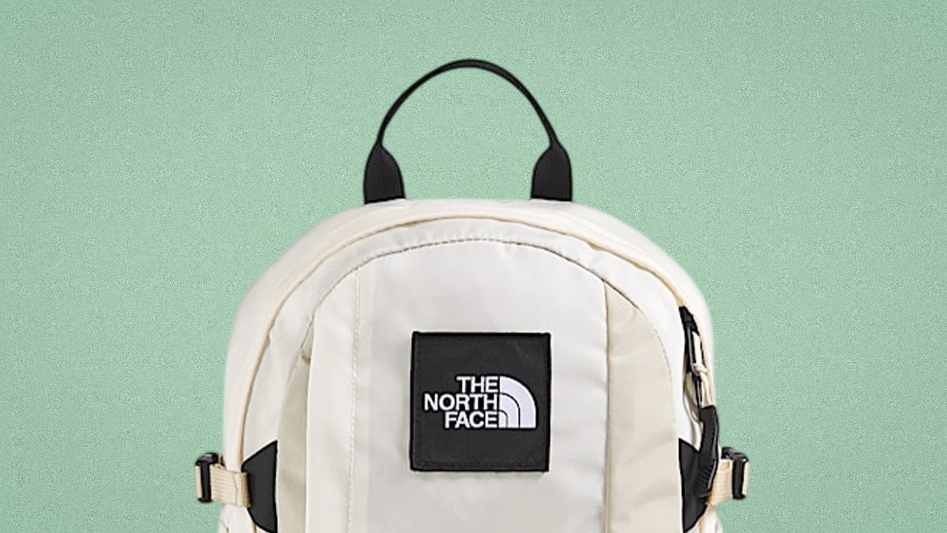 Cream-colored The North Face backpack with black logo patch and black handle loop.
