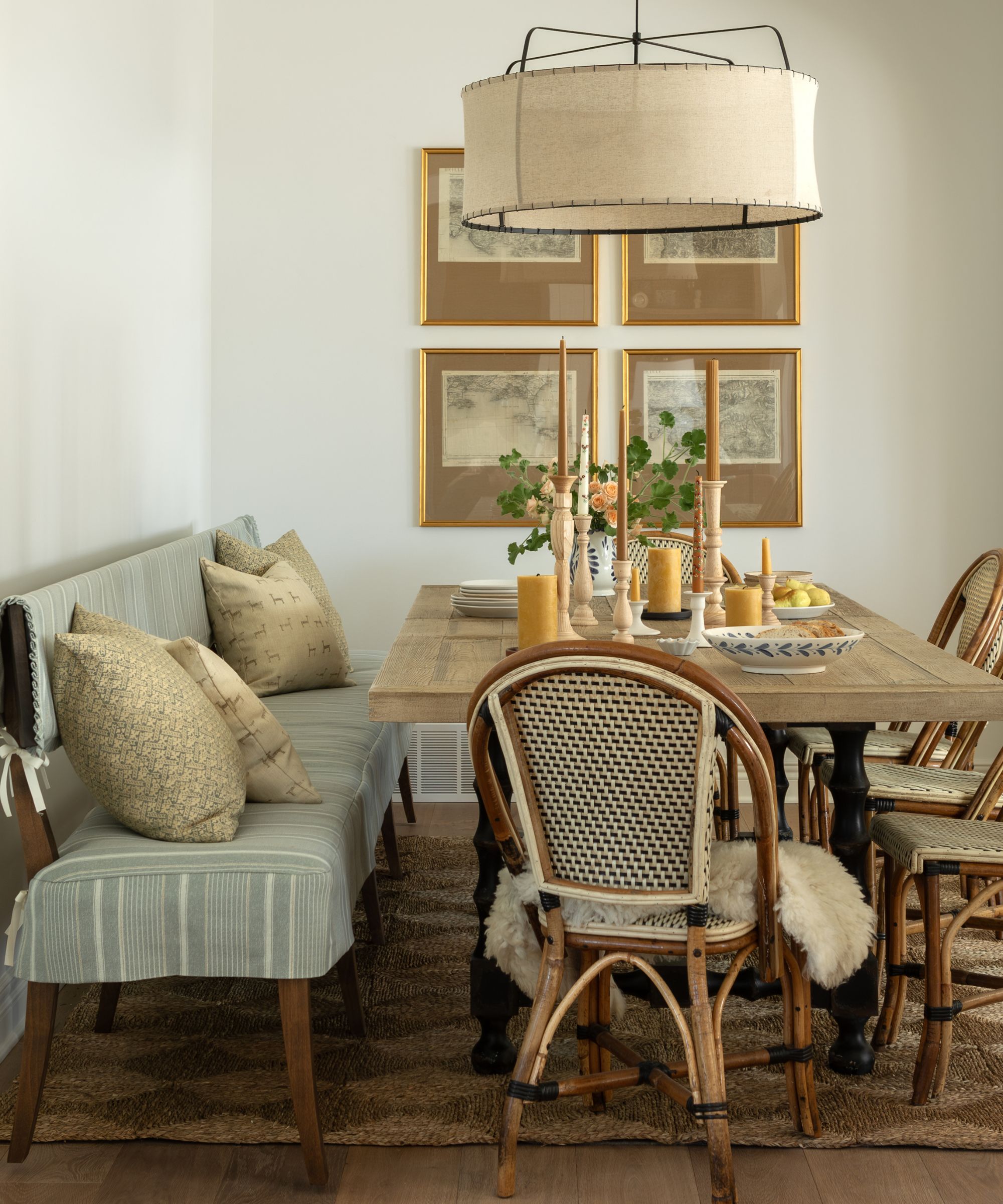 neutral dining room with an oak table, french bistro chairs, 4 vintage prints on the wall, a dining bench with blue and white striped upholstery