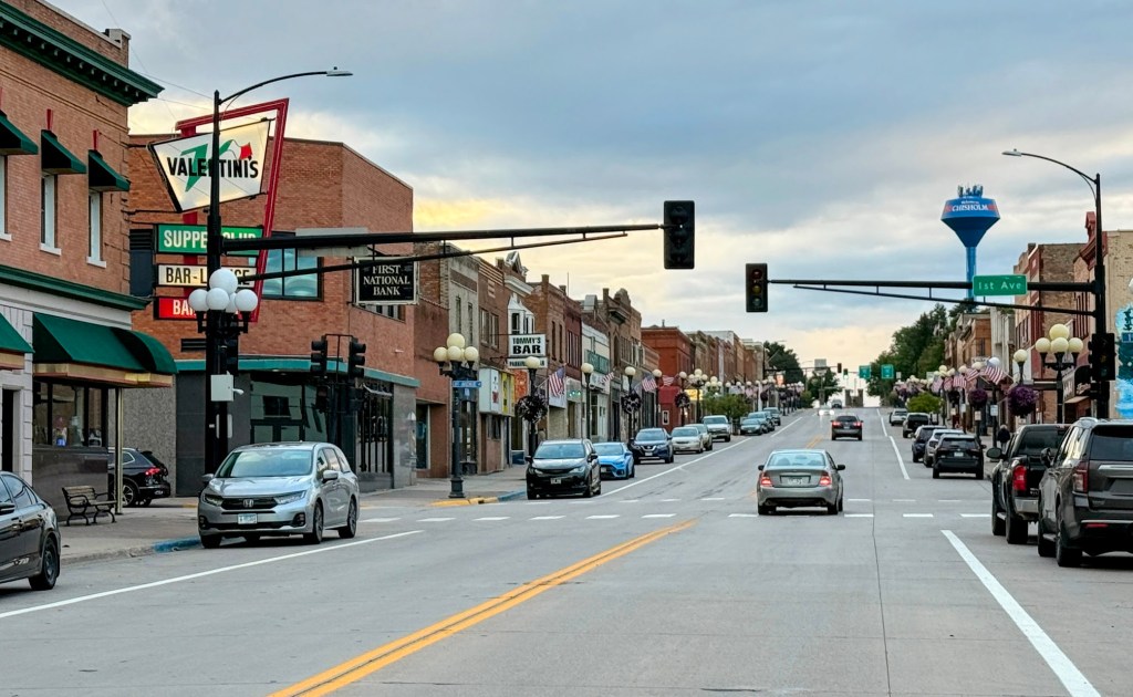 A street view of downtown Chisholm, Minnesota, features the neon sign for Valentini's Supper Club and the blue water tower in the distance.