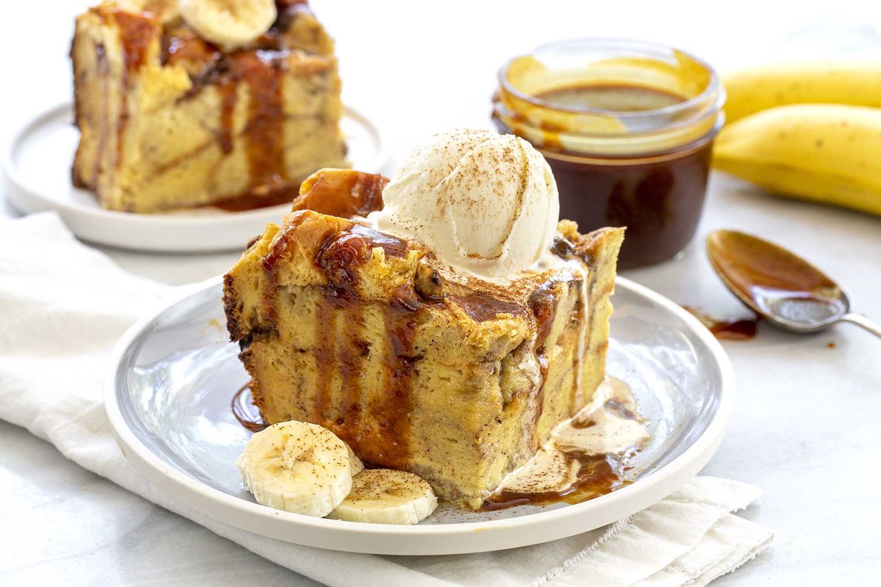 Two plates of banana bread pudding with ice cream on top, next to a jar of sauce.