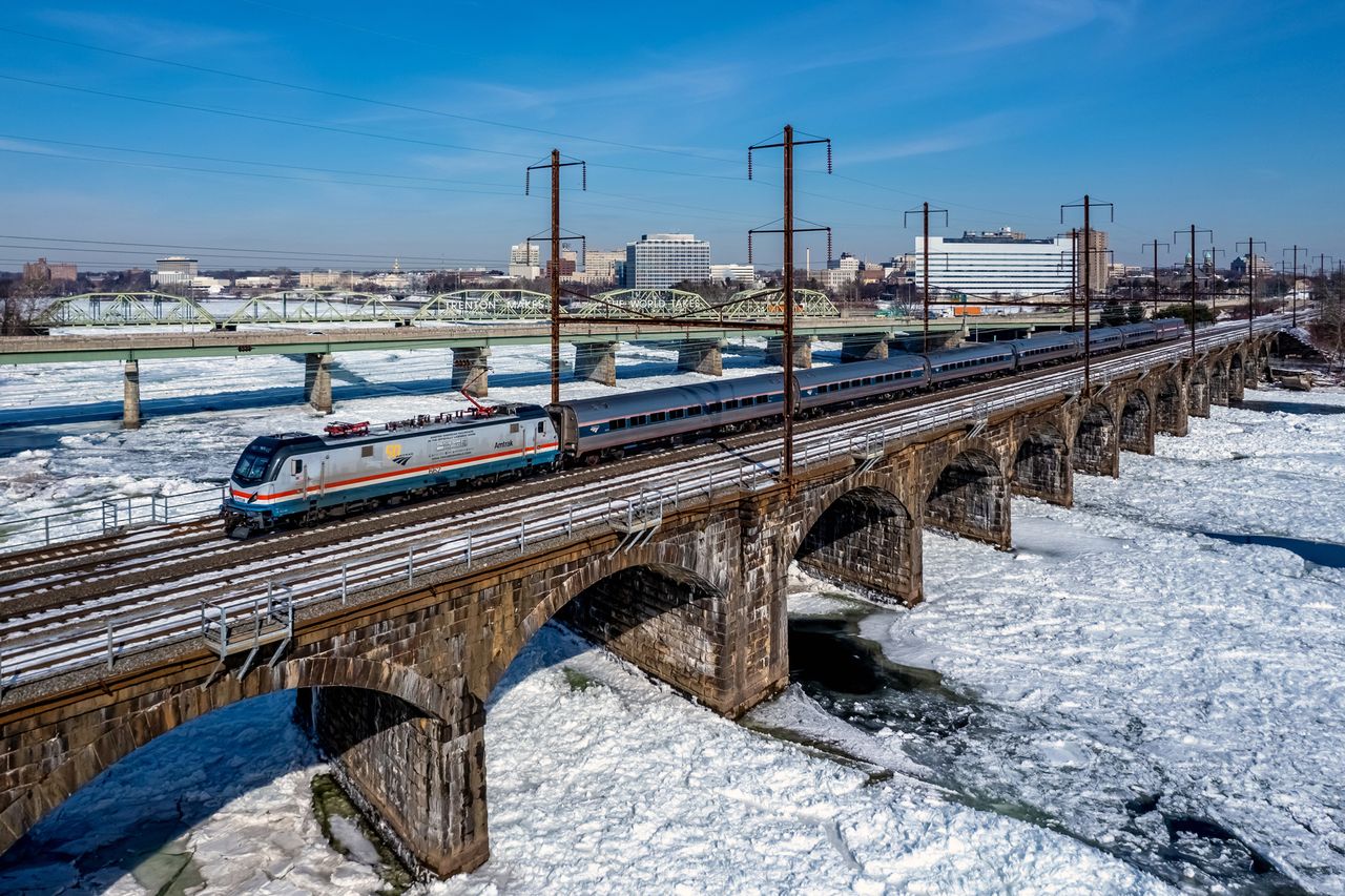 A train travels across a viaduct over a frozen river next to a cityscape
