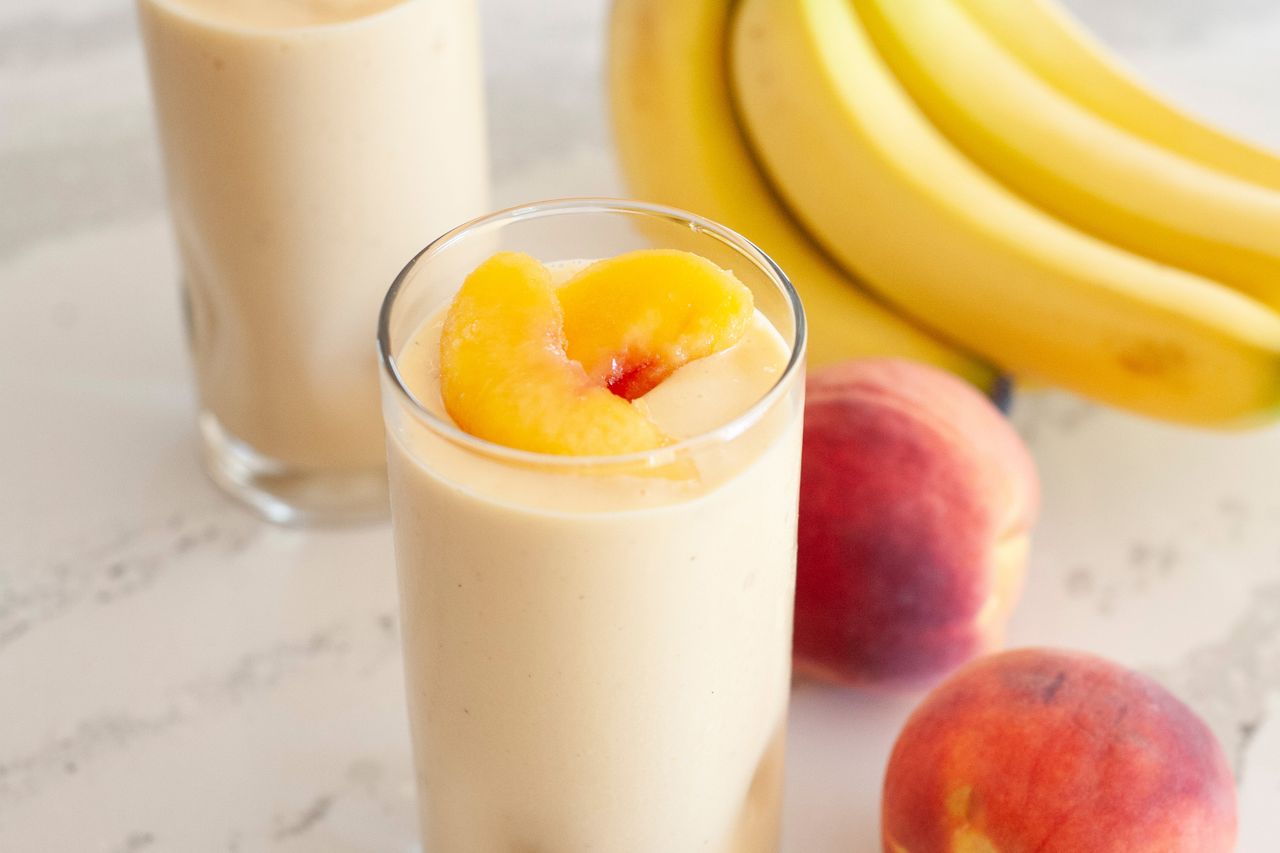 Peaches ânâ cream smoothie topped with sliced peaches and fresh fruit and a second smoothie around the glass.