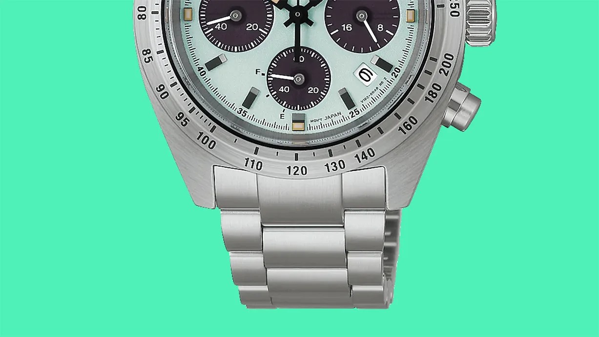 Close-up of a silver stainless steel watch band and lower half of a watch face with black subdials on a light blue background.