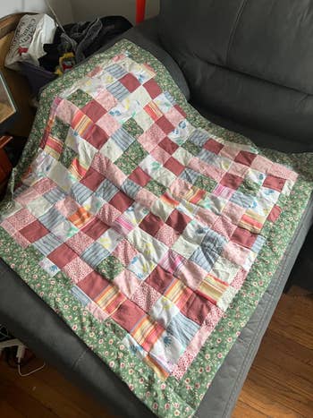 A patchwork quilt with various patterns and floral border is draped over a gray couch