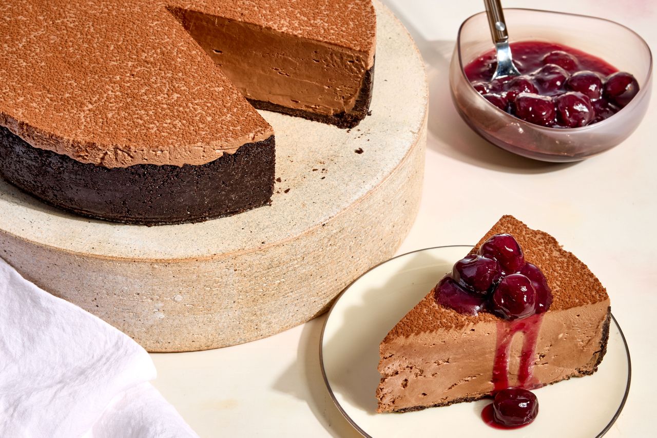 no-bake chocolate cherry cheesecake with a slice cut out and a bowl of cherries for topping.