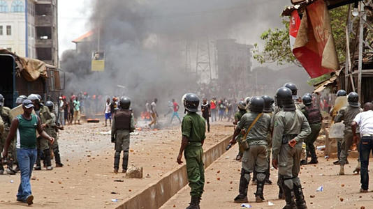 In this photo taken on Monday, April 13, 2015, Guinea security forces, center, face people rioting and burning rubbish and other goods in the streets of Conakry, Guinea.