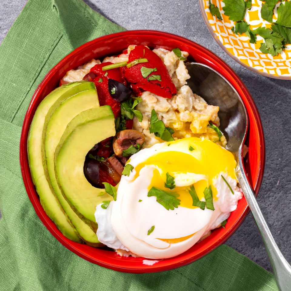 Savory oatmeal bowl topped with avocado slices roasted vegetables a poached egg and herbs placed on a green napkin