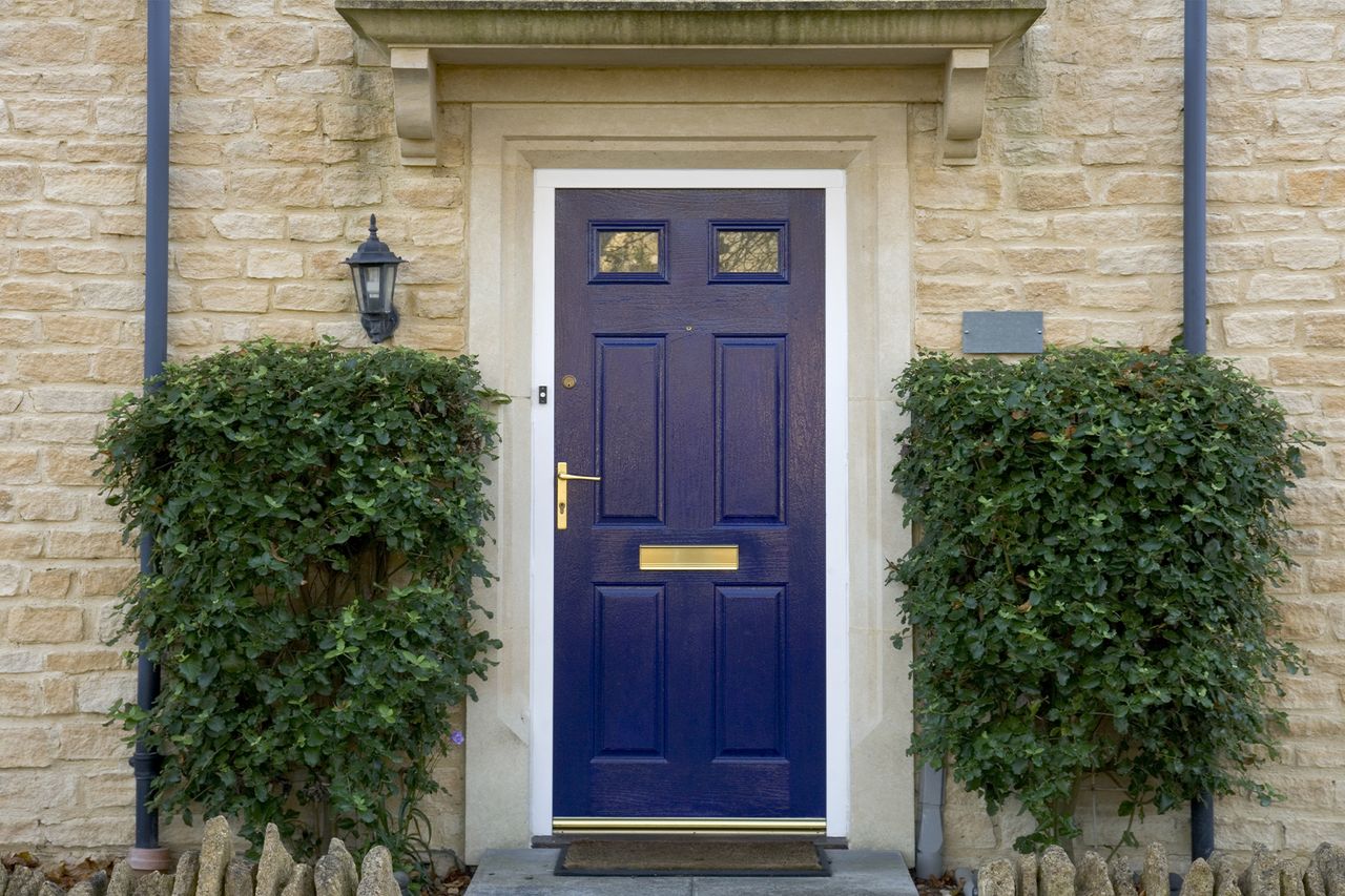 navy front door on a brick house with bushes