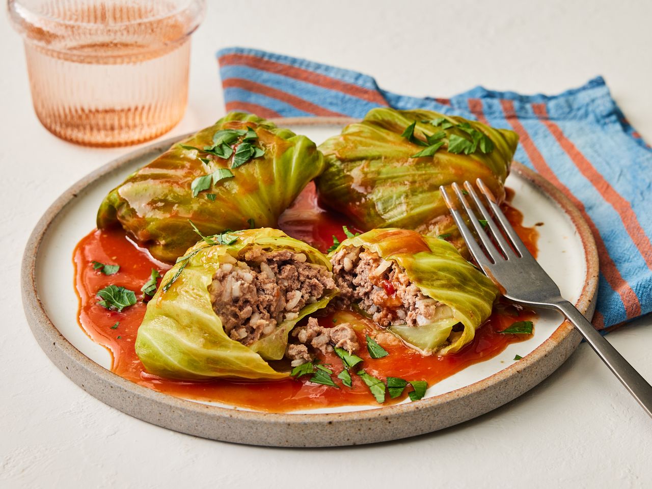 A plate of cabbage rolls, filled with meat and rice, served drizzled with tomato soup and garnished with chopped parsley