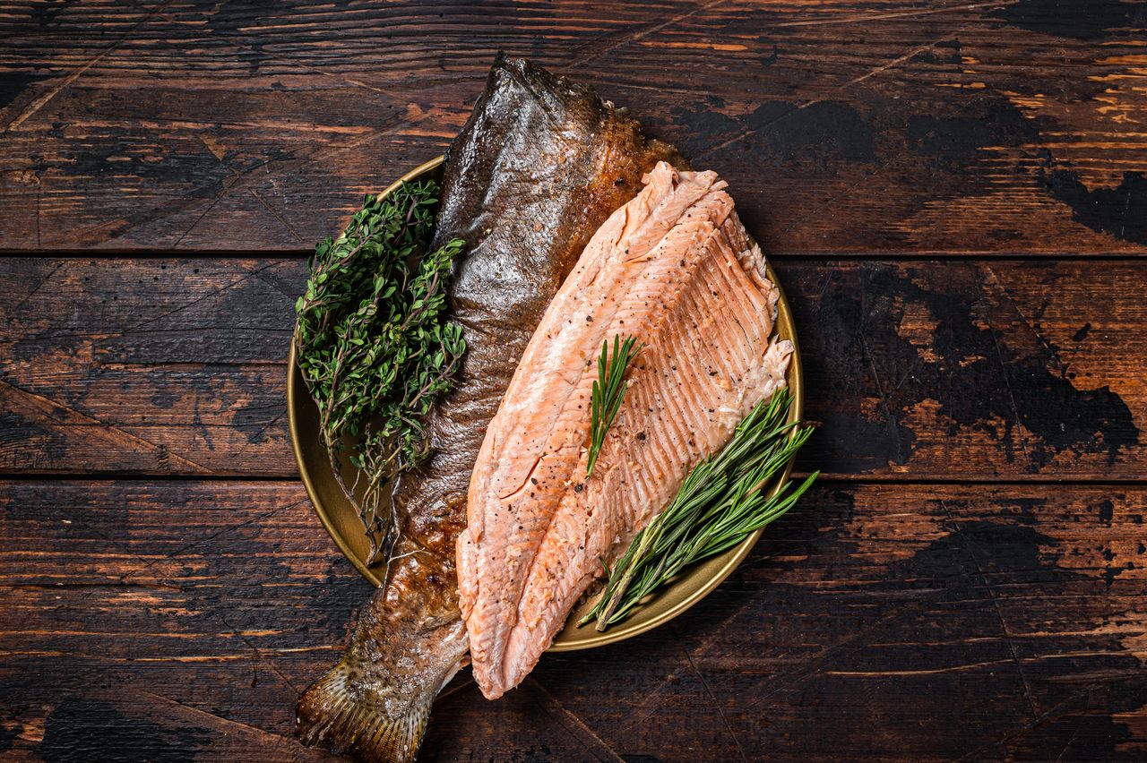 A plate with a raw whole fish a fillet and fresh herbs on a wooden surface