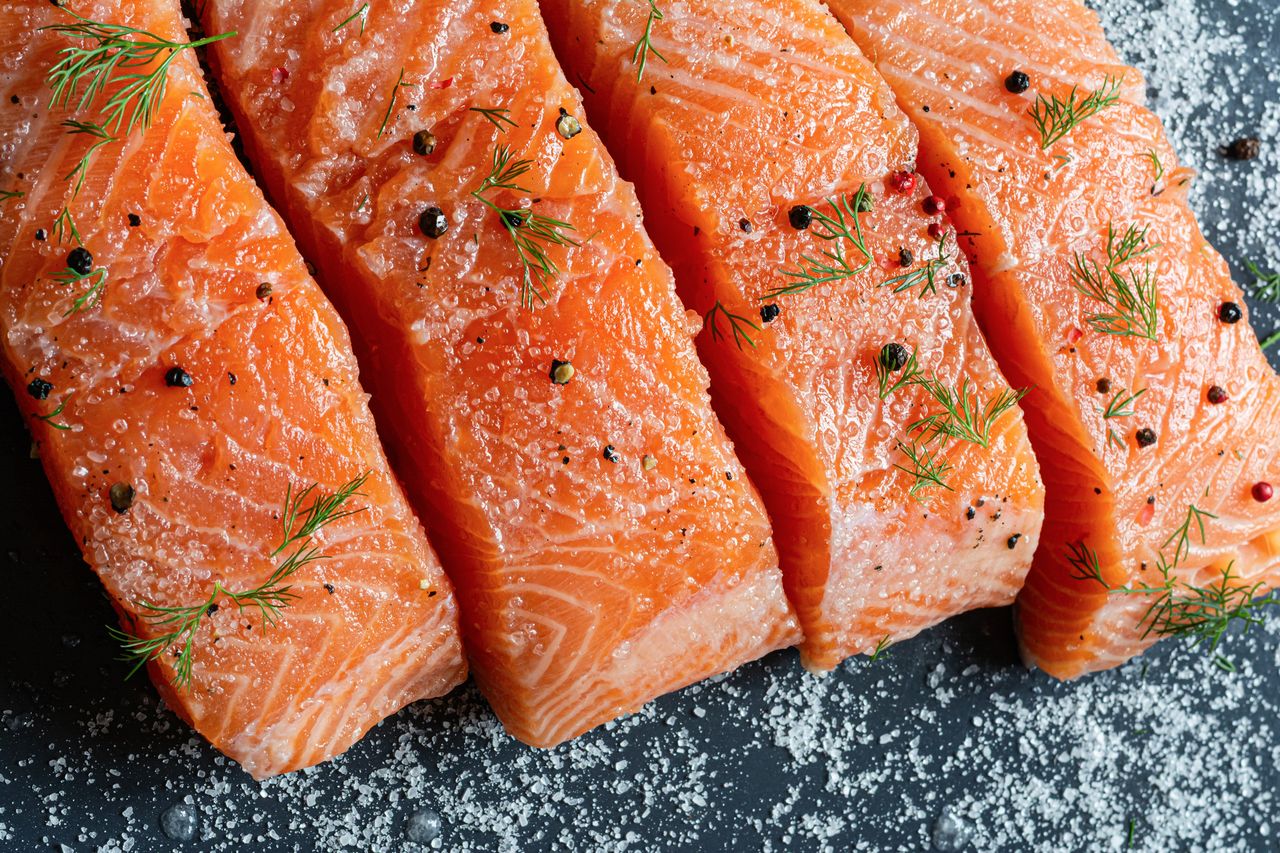 Closeup of raw salmon fillets seasoned with salt dill and peppercorns