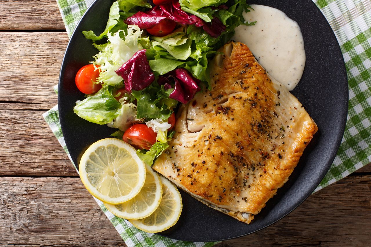 A plate with grilled fish a salad and lemon slices on a rustic table