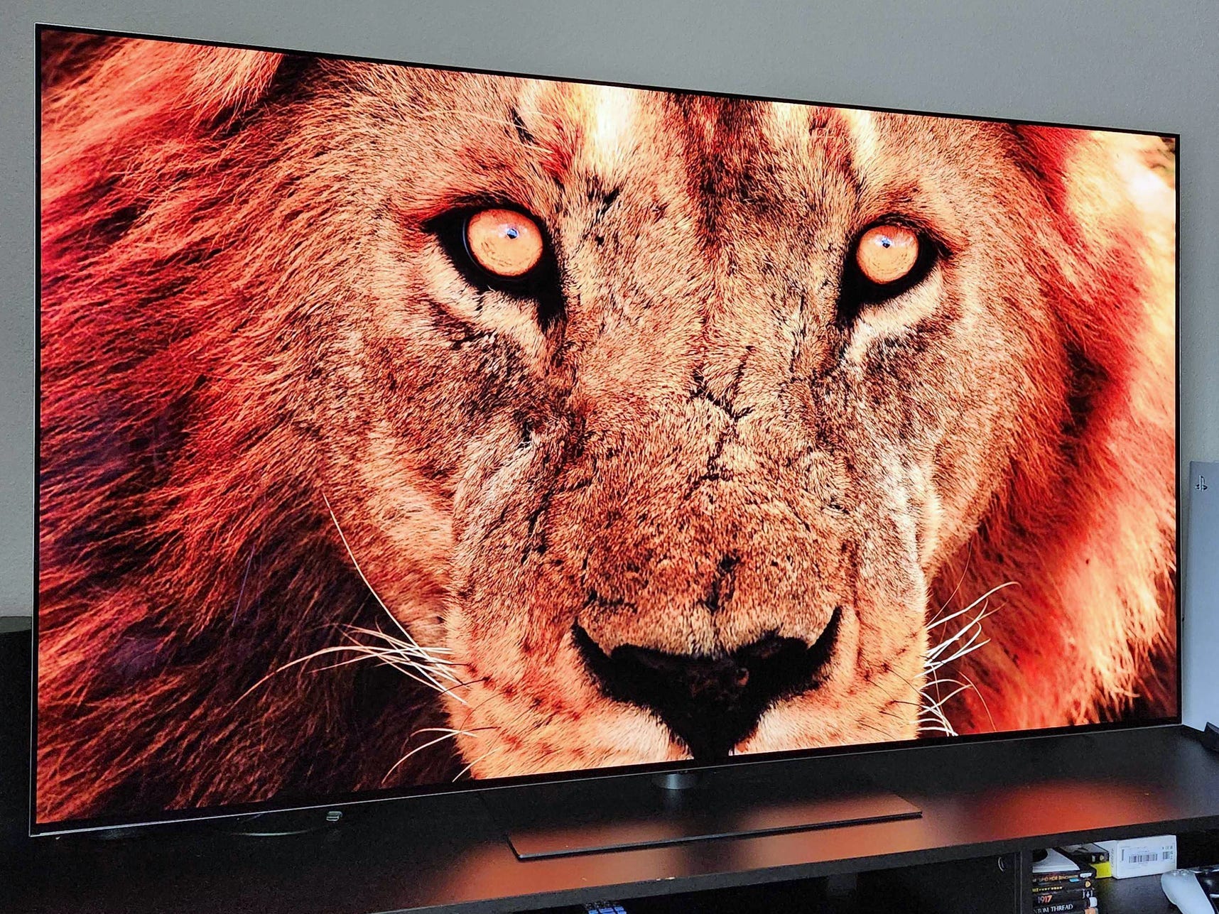 An Angled view of an LG G5 OLED TV on a media console displaying a close-up image of a lion's face.