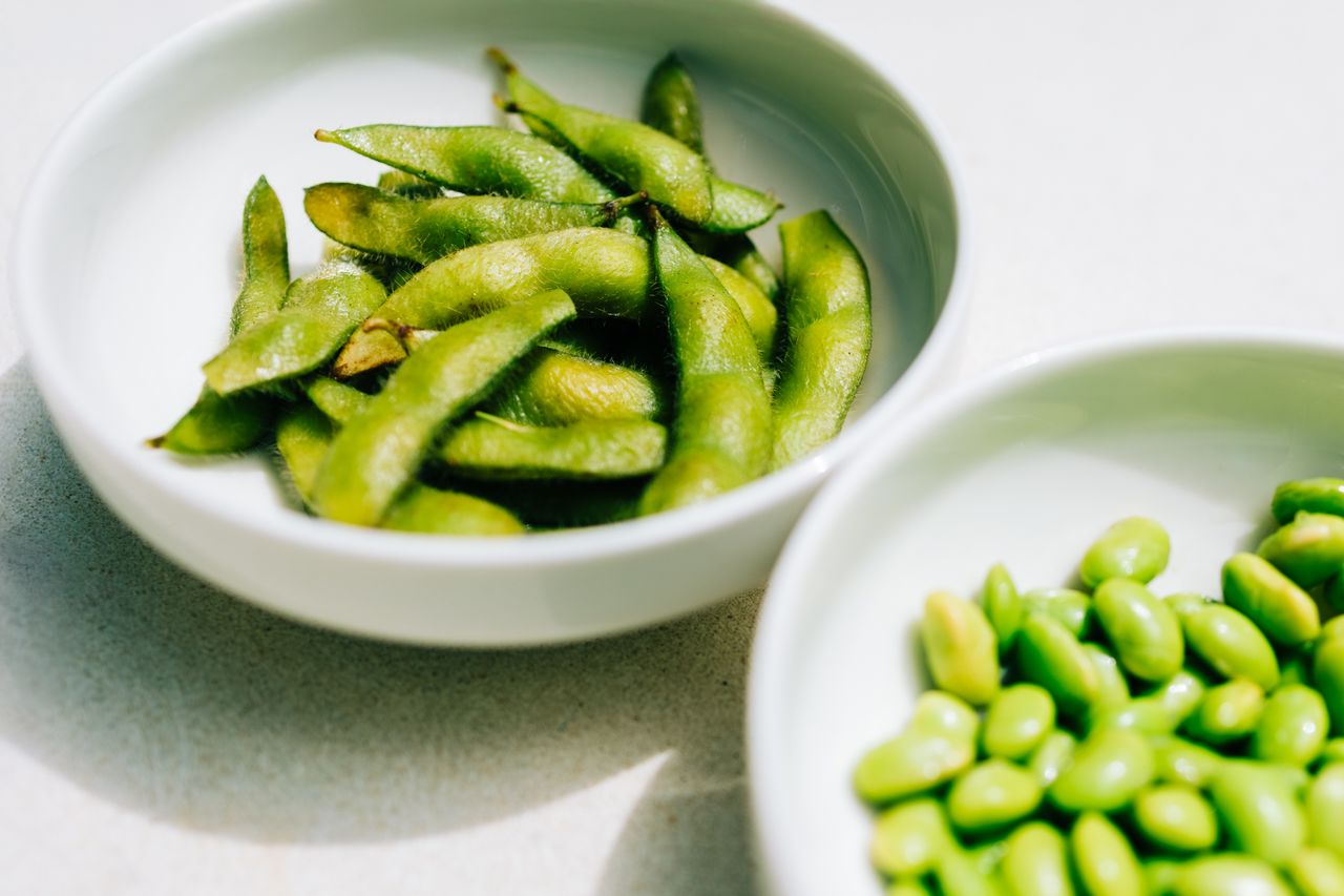 Edamame beans and pods in white bowls on light background