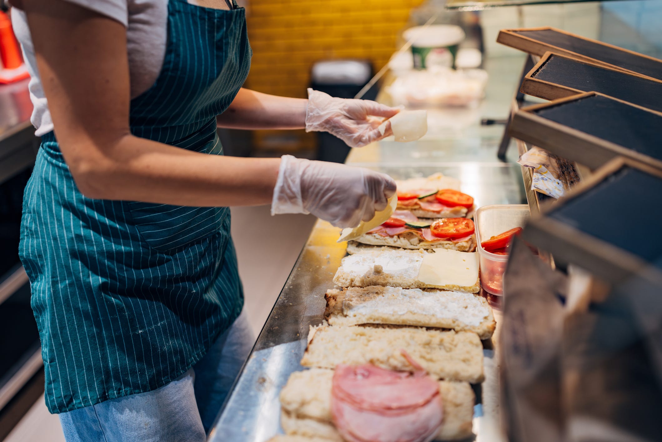 Unrecognizable female food service worker preparing fresh sandwiches at a fast food counter.