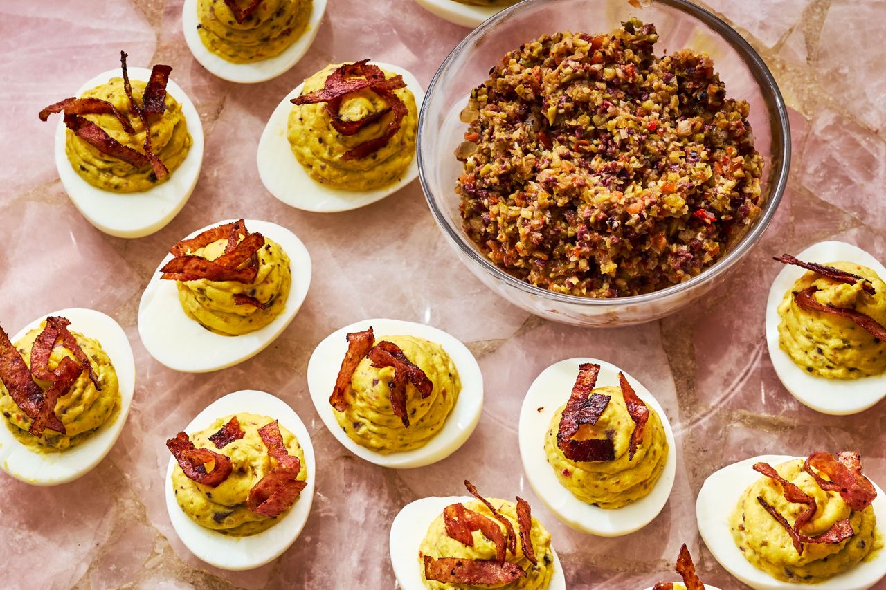 several Muffuletta Deviled Eggs on a surface with a bowl of olive salad