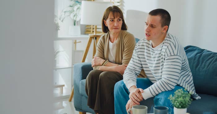 Two people sitting on a couch; the older woman looks concerned, while the younger person talks, appearing thoughtful