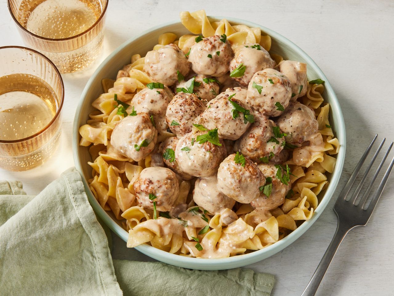 A bowl of slow cooker Swedish meatballs served over noodles and topped with chopped parsley
