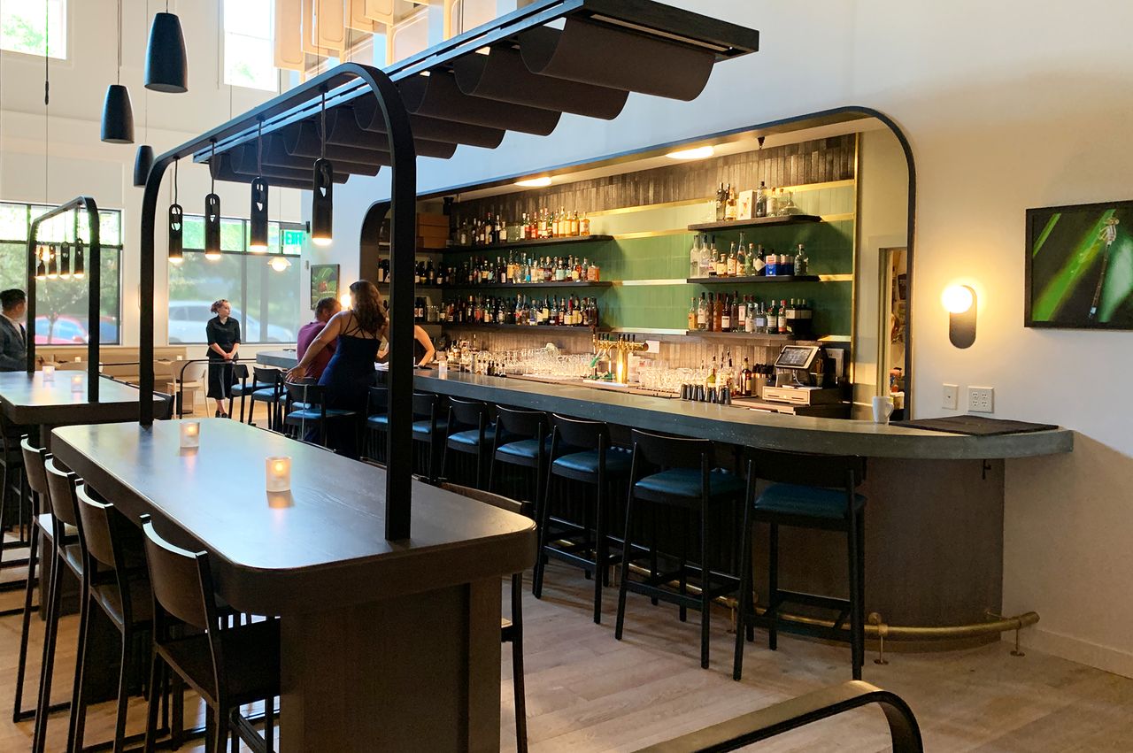 Interior of a modern and sleek bar with a few patrons seated at a counter and tables